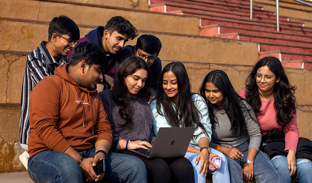 Students gathered around a laptop on campus steps at MUJ