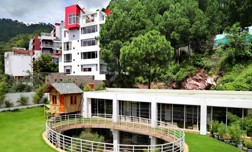 Campus buildings and lawn among pine trees at Shoolini University